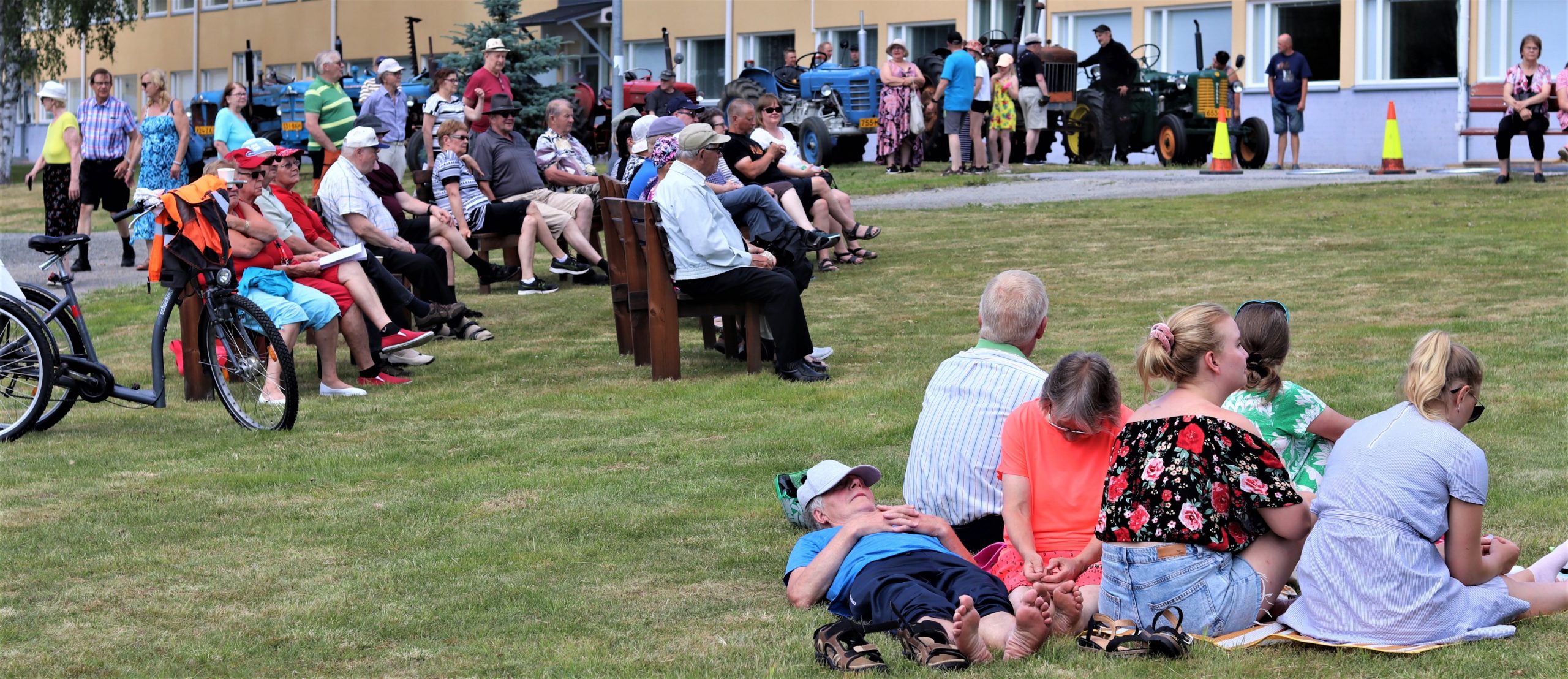 Ihmiset istuvat nurmikolla ja penkeillä seuraamaassa tapahtuman ohjelmaa.
