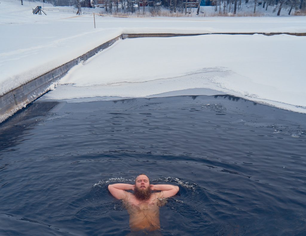 Avantomaakari Topias Tölli kelluu avannossa kädet niskan takana ja nauttii kylmästä vedestä.